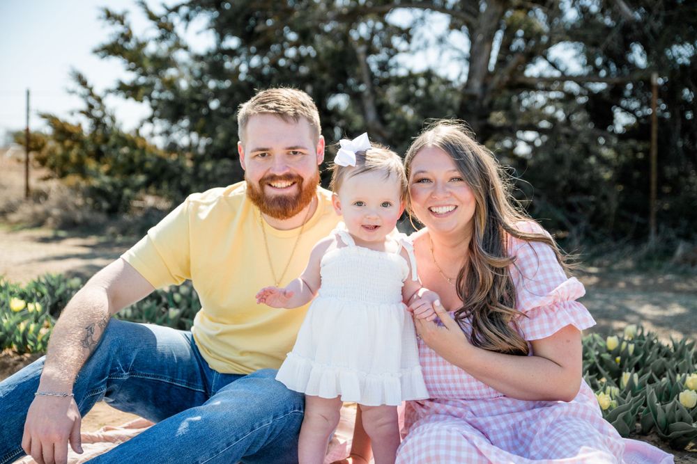 A family sits together outdoors on a sunny day surrounded by greenery and spring flowers.