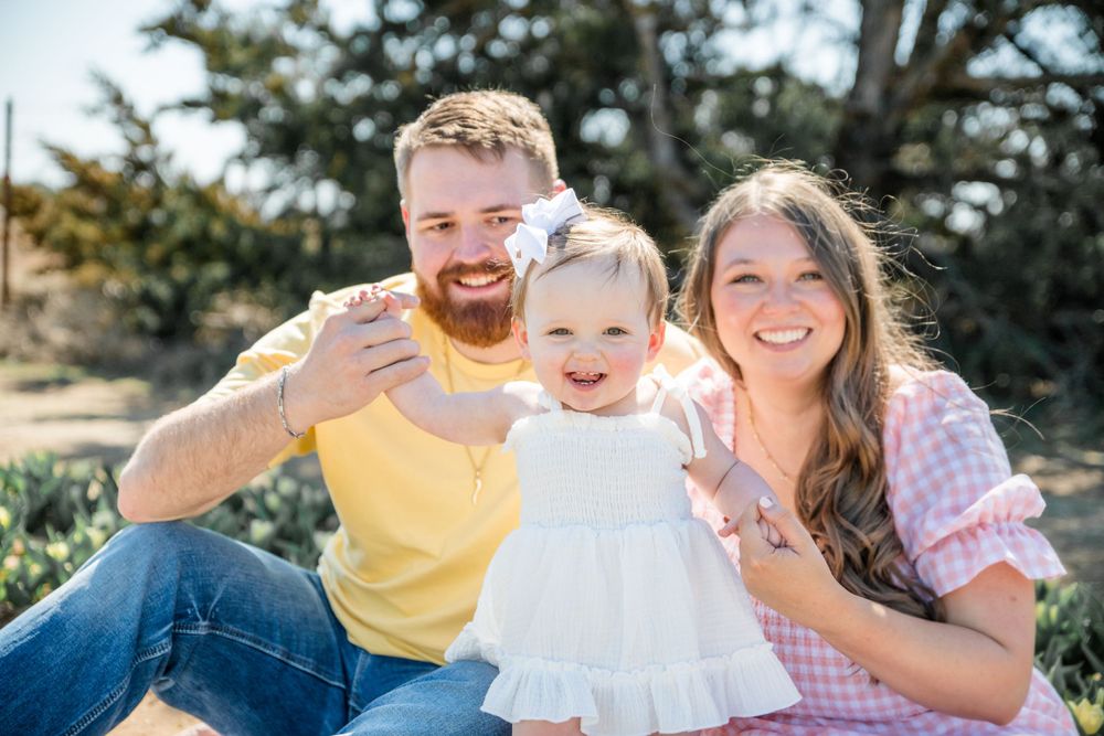 A happy family sitting together outdoors on a sunny day, smiling and waving at the camera.