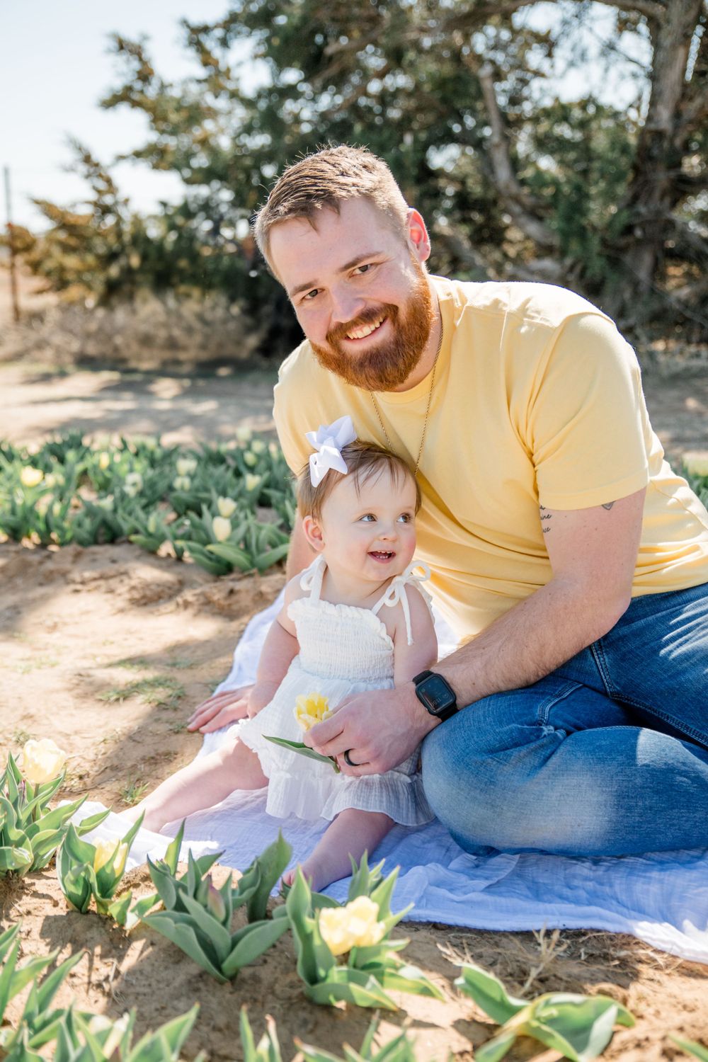 A parent and child share a tender moment while sitting among blooming yellow flowers in a garden setting.