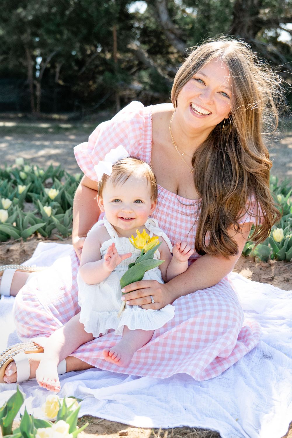 Loving moment captured outside on a picnic blanket with gingham dress and baby in sunlit garden setting.