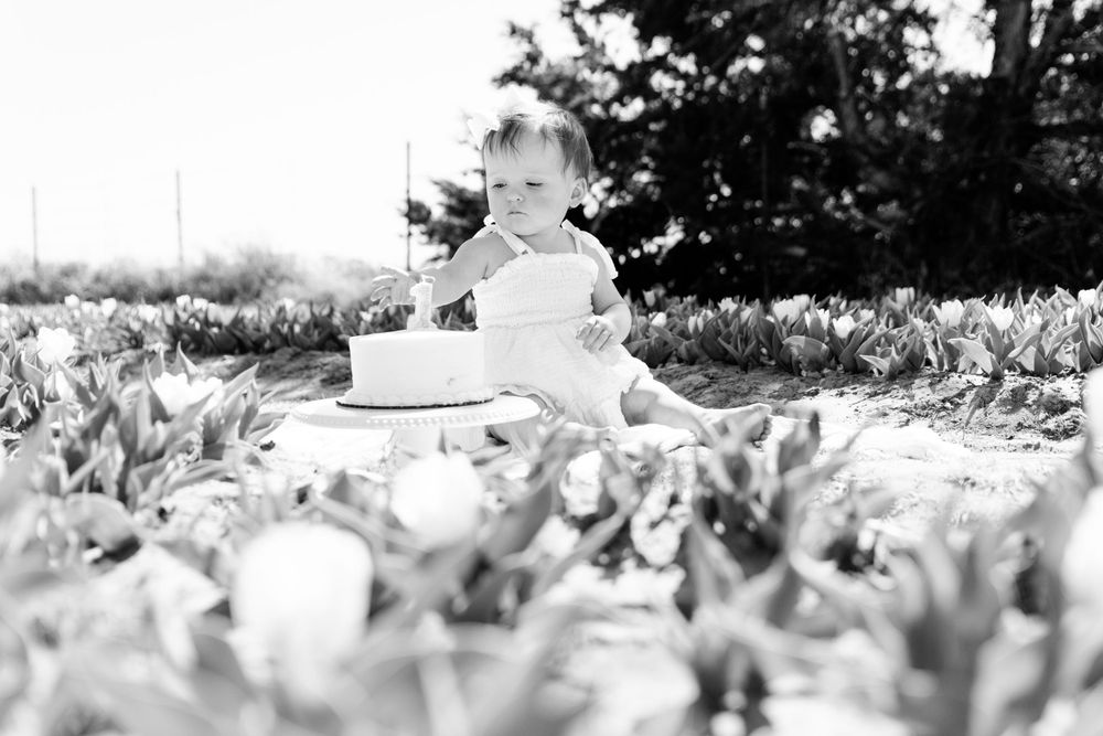 Black and white photo of a child sitting outdoors surrounded by autumn leaves in a garden setting.