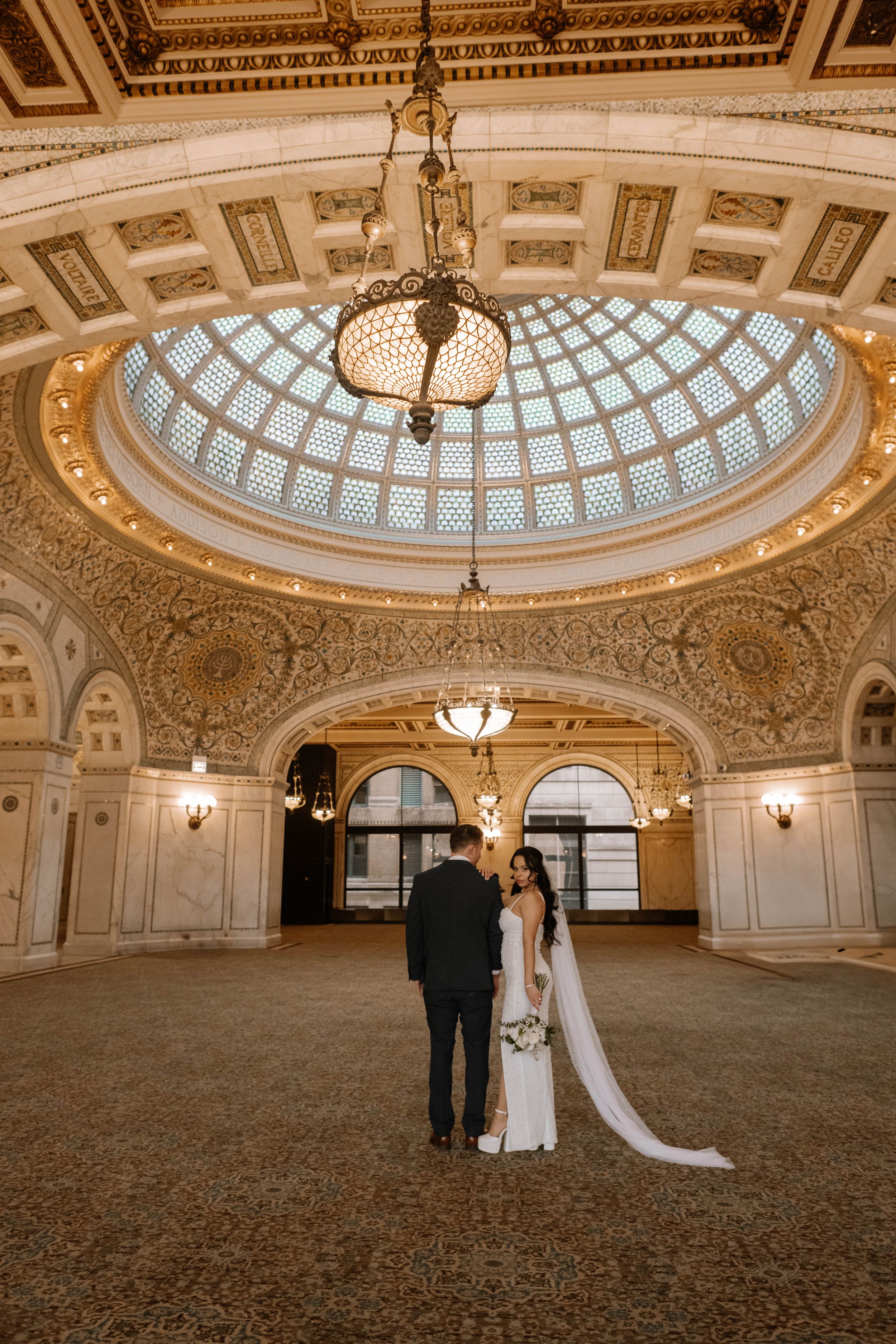 A couple standing beneath an ornate domed rotunda with glass ceiling and classic architectural details at the Chicago Cultural Center.