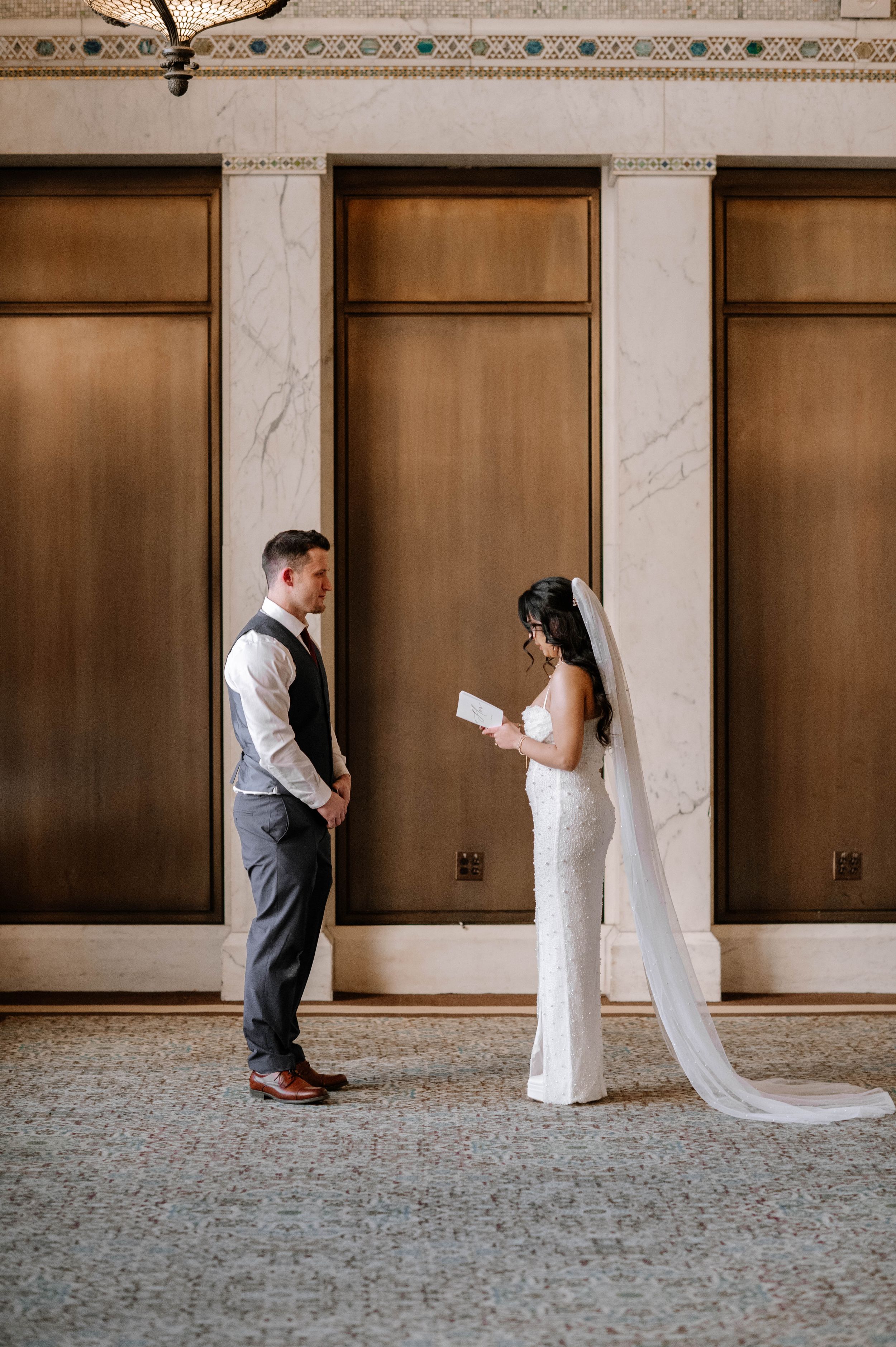 A tender first look moment between a couple on their wedding day in an elegant hallway with marble walls.