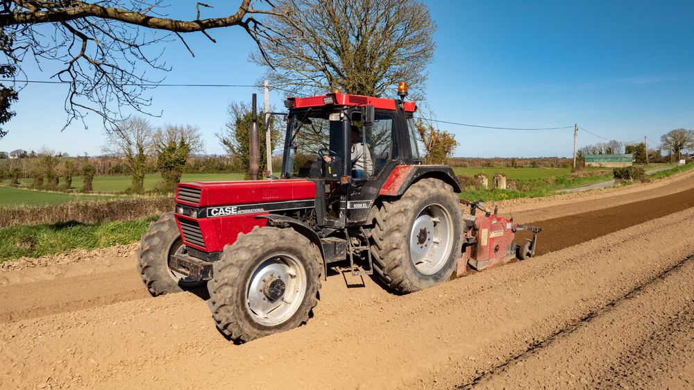 Panoramic view of tractors plowing agricultural fields in spring with bare trees in the background.