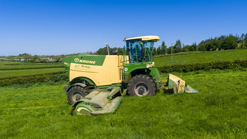 A panoramic view of green farmland with agricultural machinery and tractors working in the rolling fields.