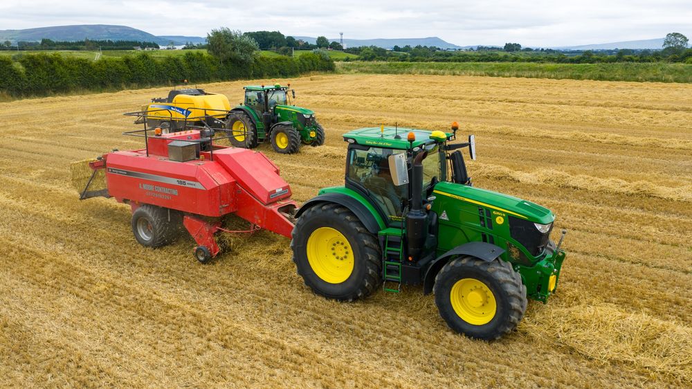 Three tractors working in a harvested wheat field with one pulling a red baler on rolling agricultural landscape.