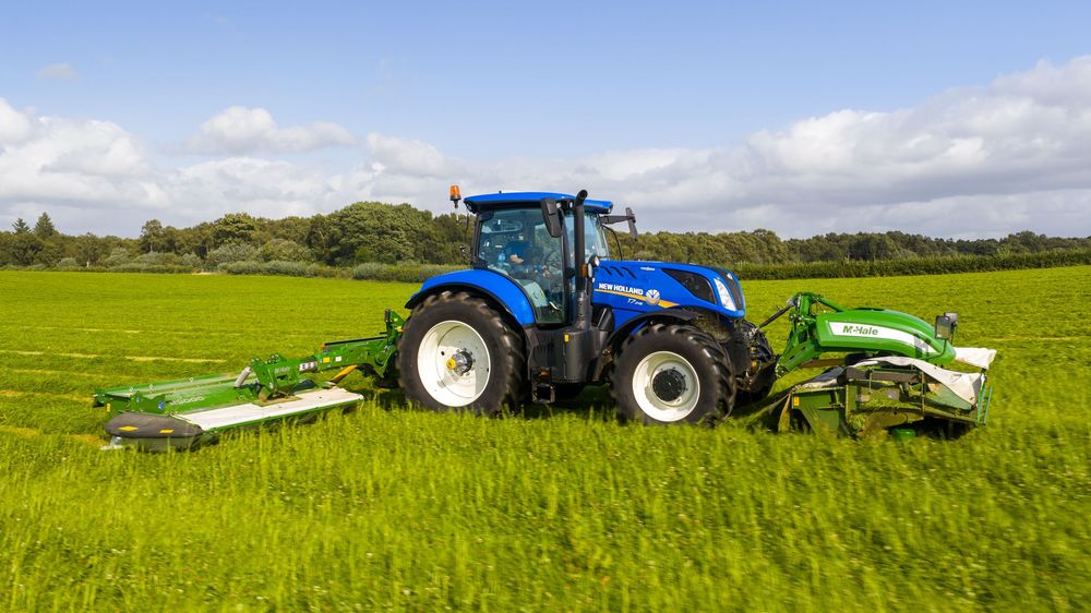 Modern farm tractors working in lush green fields under a bright blue sky with white clouds.