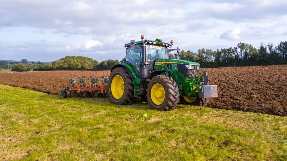 A panoramic view of agricultural fields with tractors working on plowing and preparing farmland under cloudy skies.