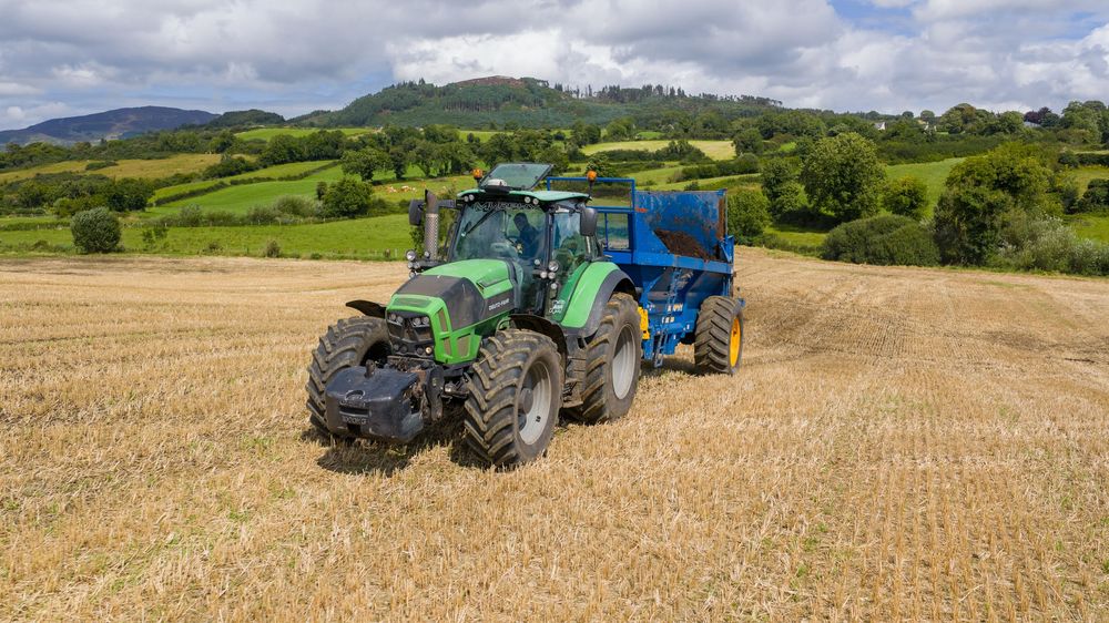 A panoramic view of agricultural fields with tractors working on harvesting or plowing under a cloudy sky.