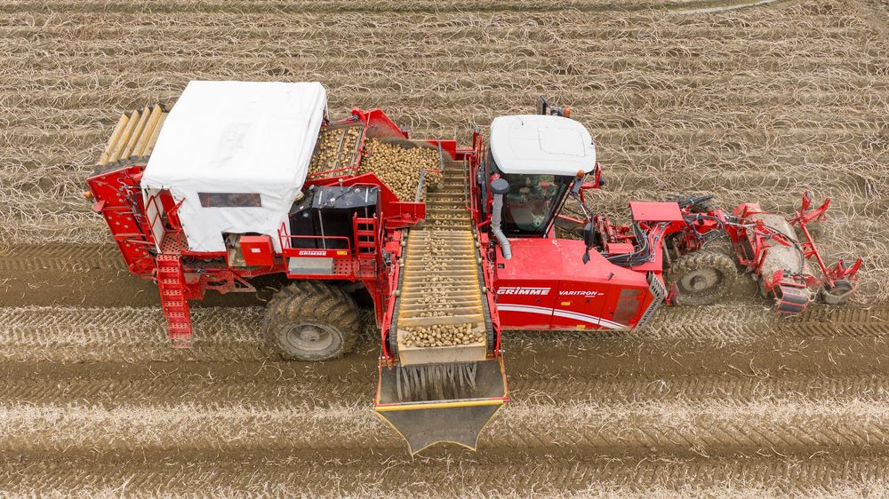 Aerial view of red agricultural machinery harvesting crops in a field showing multiple farming operations in sequence.