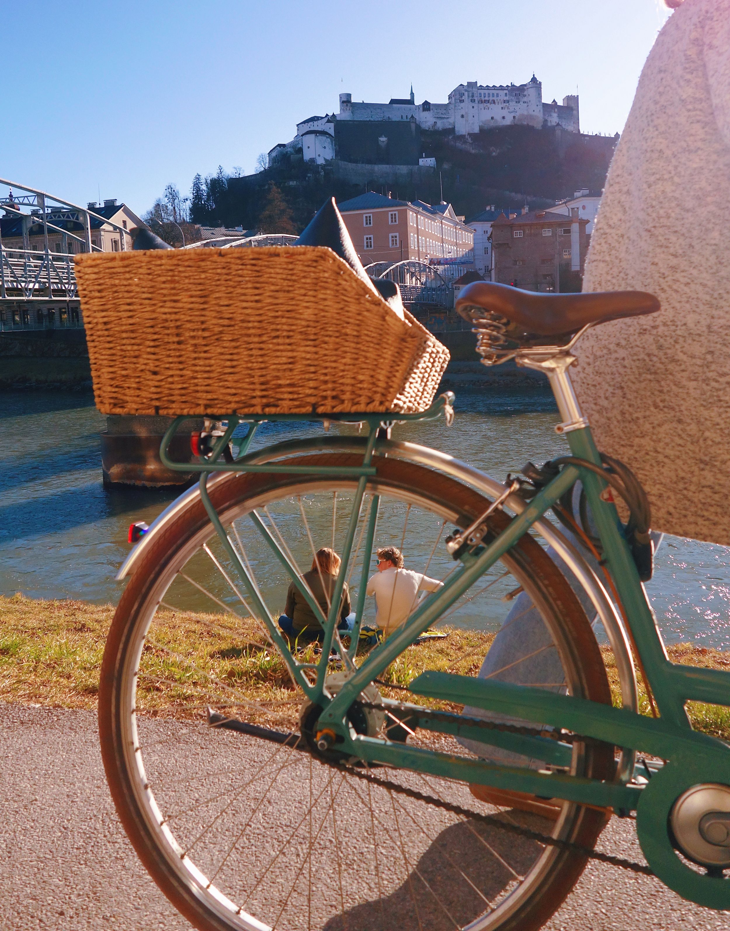 Vintage bicycle with wicker basket parked against backdrop of historic Salzburg Castle on hilltop in Austria.