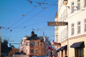 Historic building with ornate architecture and overhead tram wires along a street in sunny weather against blue sky.