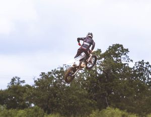 Dirt bike rider performing high-altitude jump against cloudy sky.