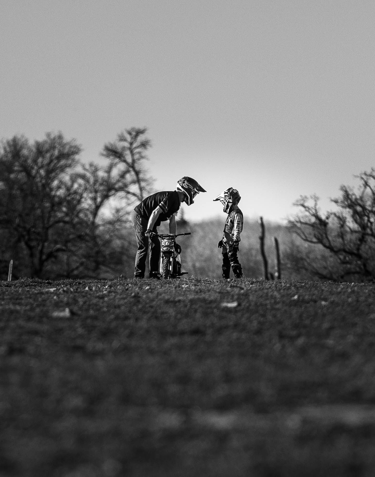 Silhouetted figures sharing a moment on dirt bikes at sunset.