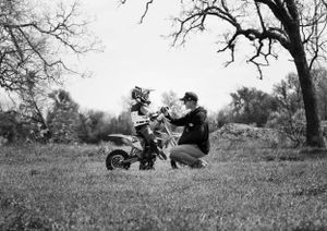Black and white photo showing dirt bike lesson or training session in rural setting with trees.