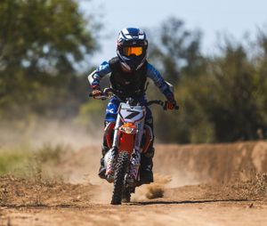 Dirt bike rider in blue gear kicking up dust while racing on an off-road track.