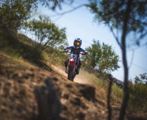 Motorcyclist riding uphill on a dirt trail surrounded by trees.