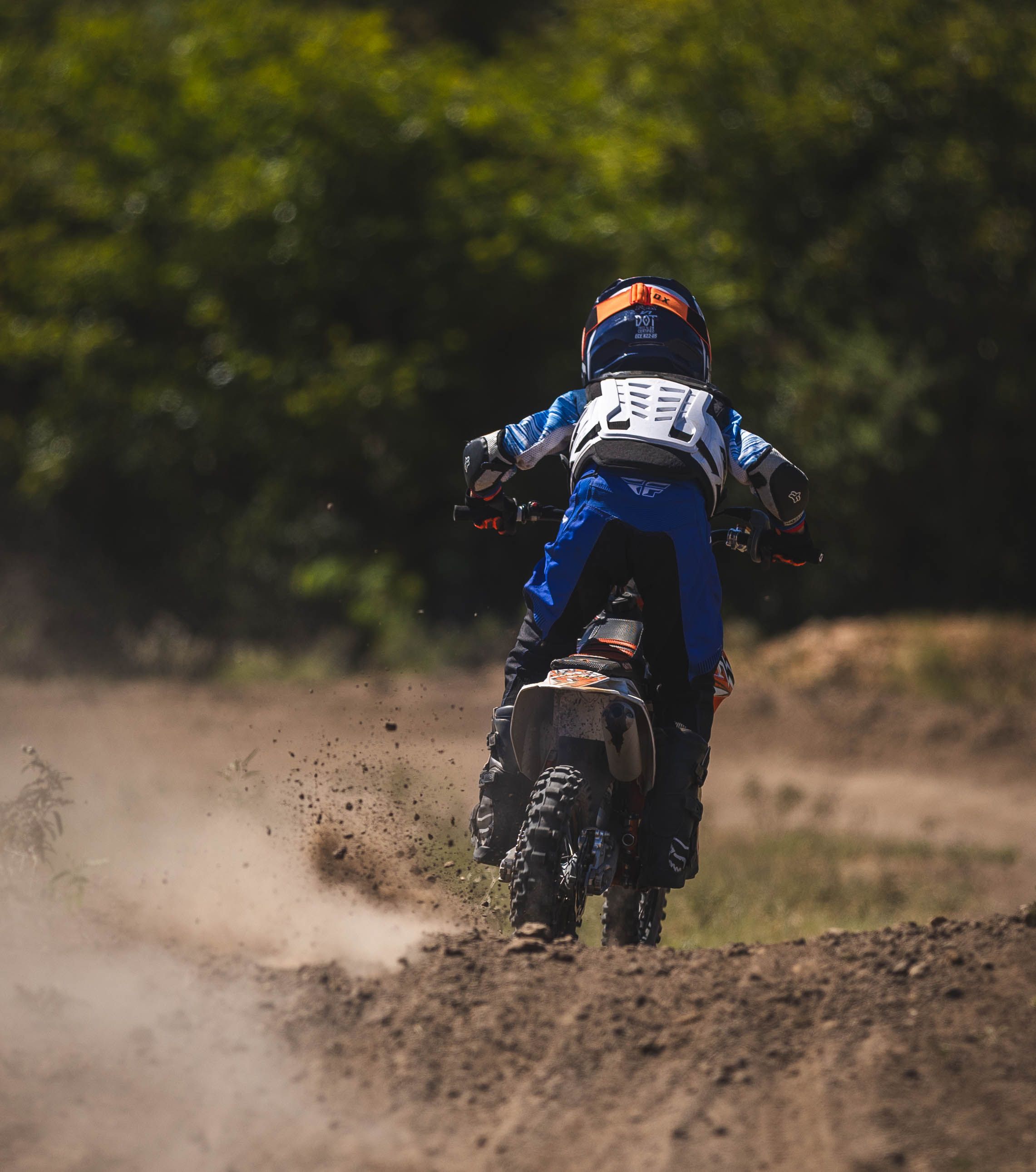 Dirt bike rider creating dust cloud while accelerating on an off-road track.