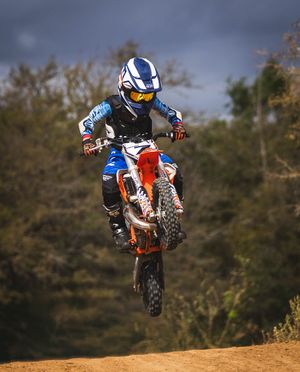 Dirt bike rider catching air off a jump wearing blue and white gear on an orange motorcycle.
