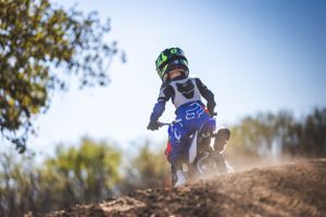 Young rider tackles dirt bike jump on motocross track during sunny day.