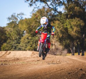 Rider airborne on red dirt bike during motocross jump on dirt track course.