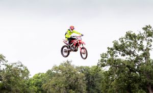Dirt bike rider in bright yellow gear soaring through the air during an off-road jump.
