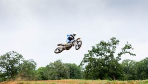 Airborne dirt bike rider performing a jump against a backdrop of trees and sky.