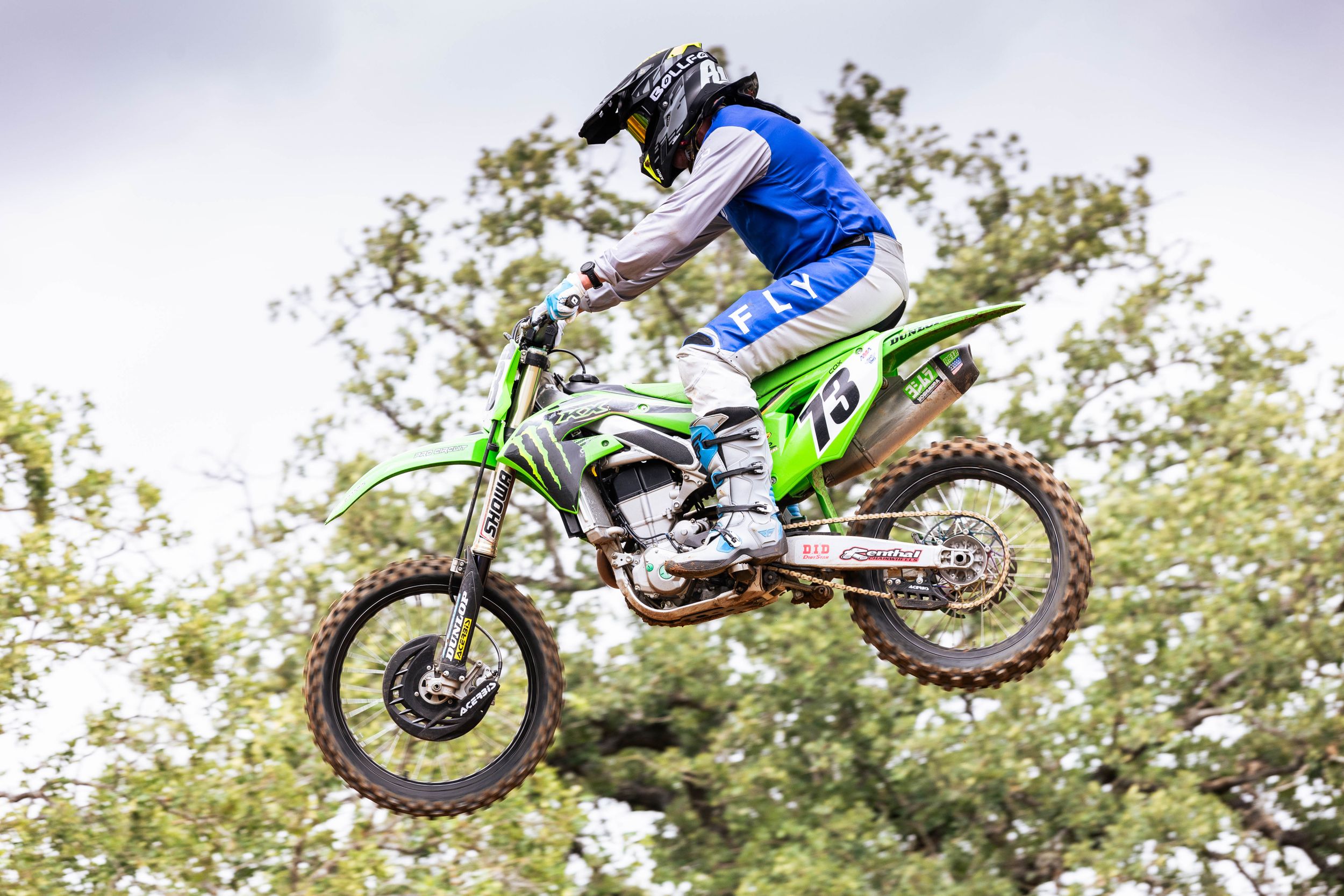 Motocross rider in blue gear performing aerial stunt on a green dirt bike.