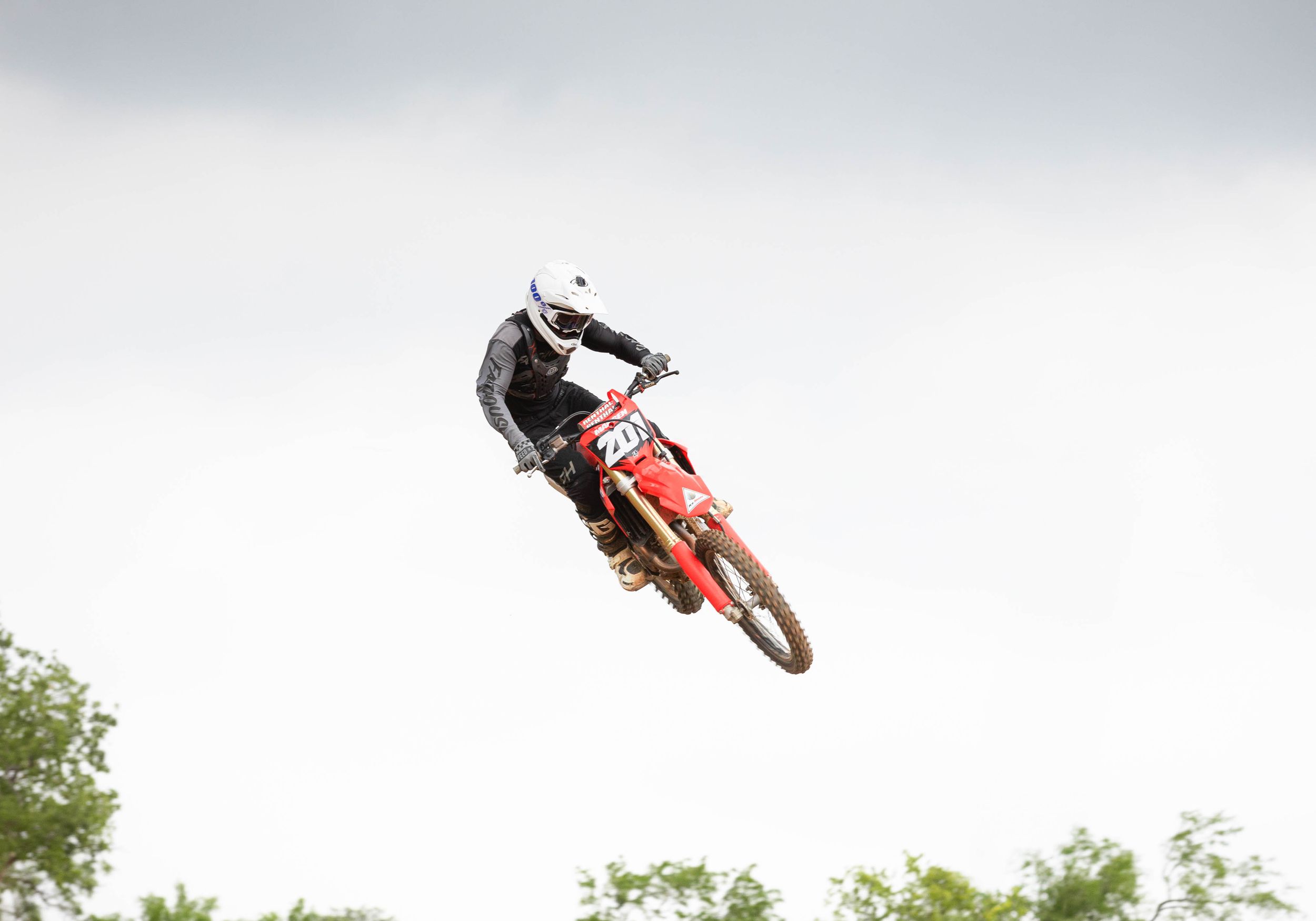 Red dirt bike and rider silhouetted against cloudy sky during mid-air jump.