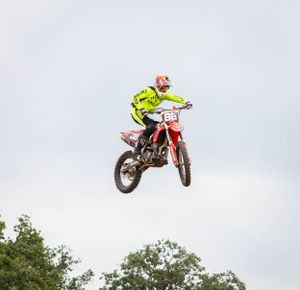 Motocross rider in neon yellow gear jumps high on dirt bike during competition.