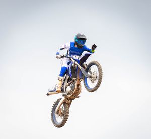 Motocross rider in blue performing aerial jump on dirt bike against grey sky background.