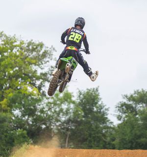Motocross rider number 26 on green motorcycle performing high jump on dirt track.