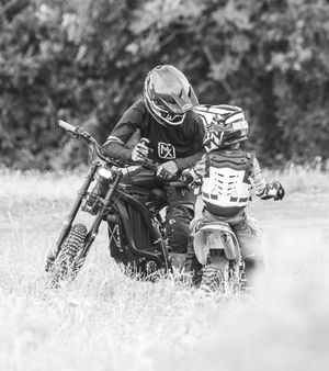 Black and white image of motorcyclist teaching young rider on dirt bikes.
