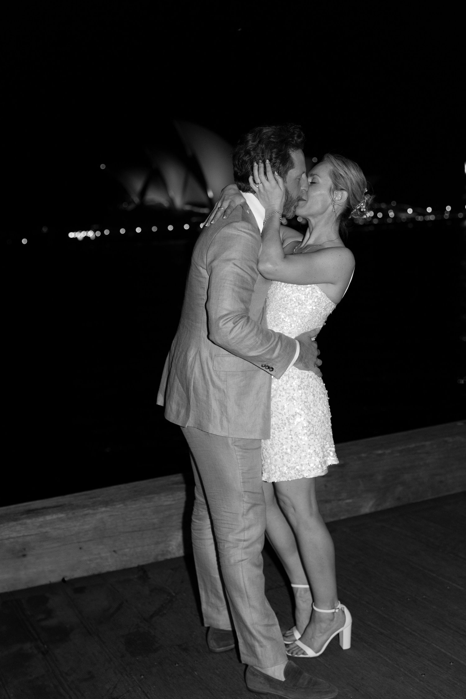 Black and white nighttime photo of couple sharing romantic moment on waterfront deck.