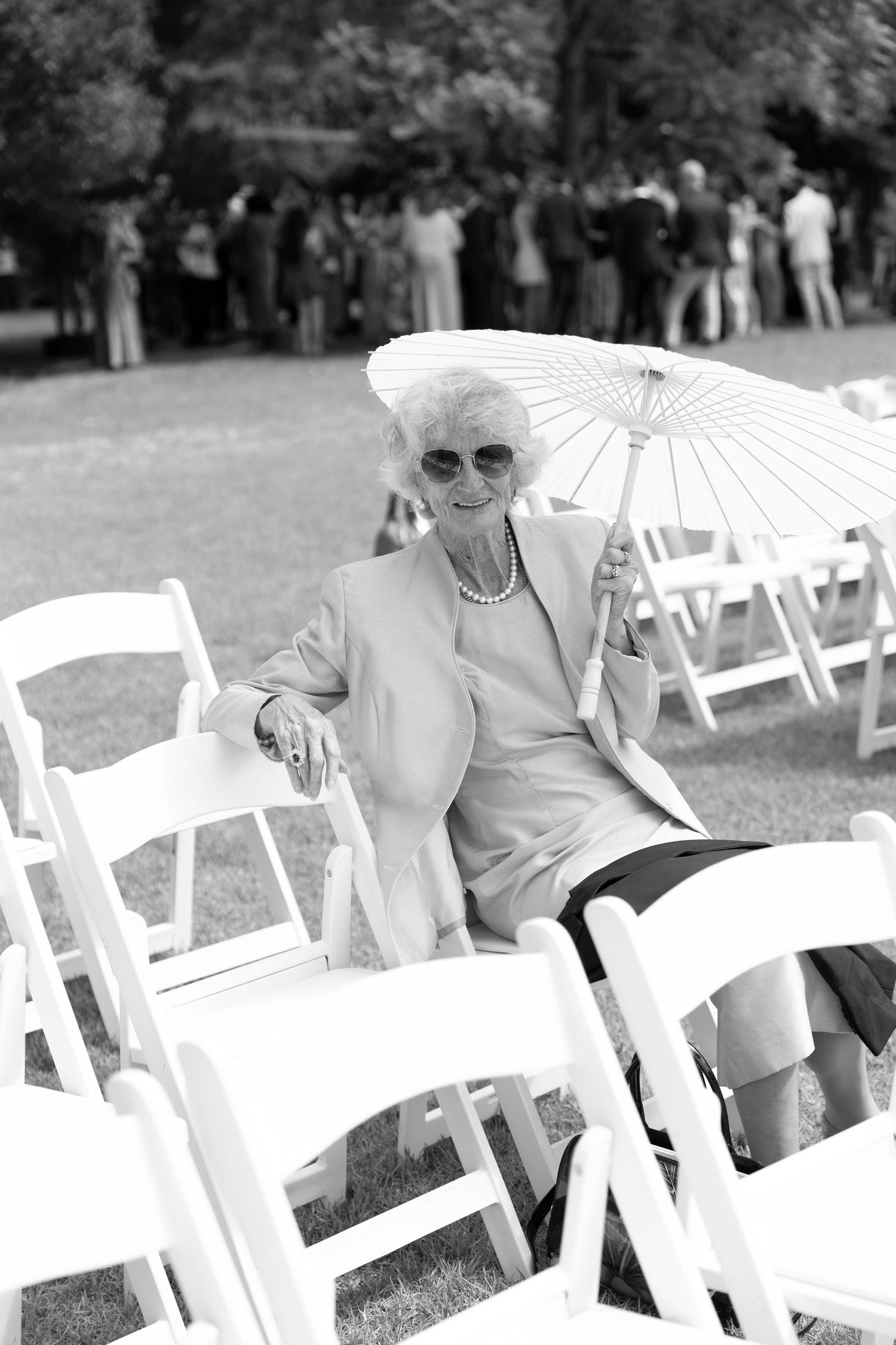 A black and white photo of an elegant guest with a parasol seated at an outdoor event.
