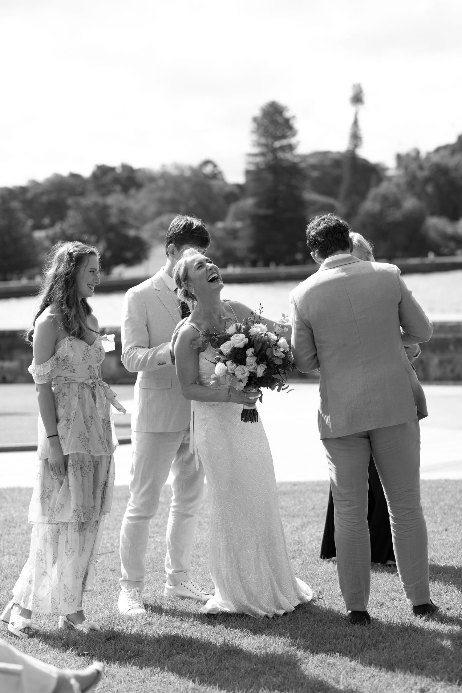 Wedding party gathered on a sunny day by the water in formal attire.