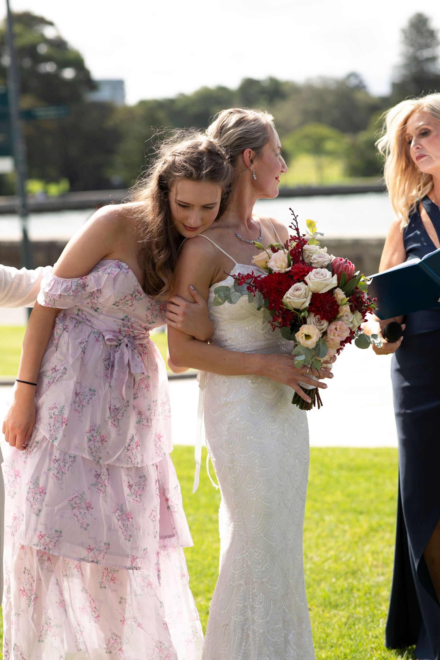 Wedding party members in pastel and navy dresses holding a vibrant red and white bouquet.