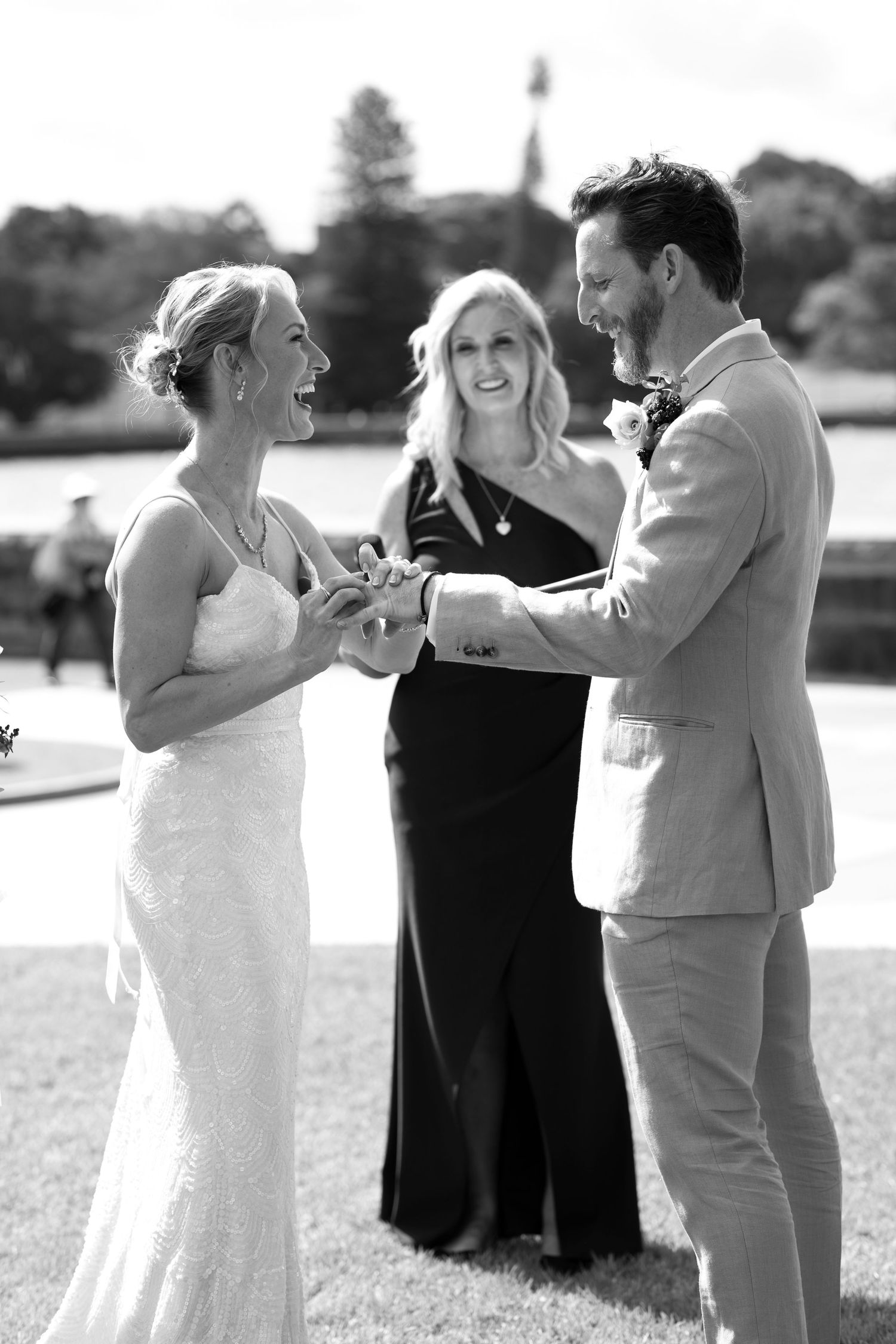 Wedding ceremony with couple exchanging rings outdoors as officiant looks on.