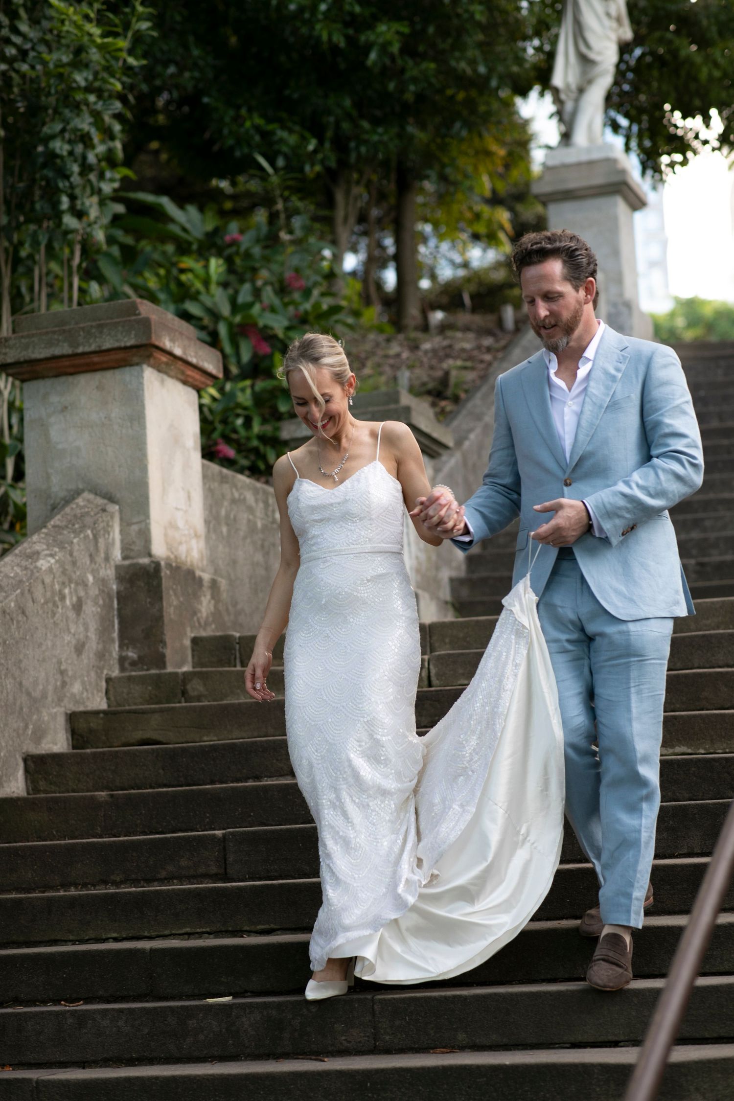 Wedding couple descending stone steps together, bride's dress trailing behind them.
