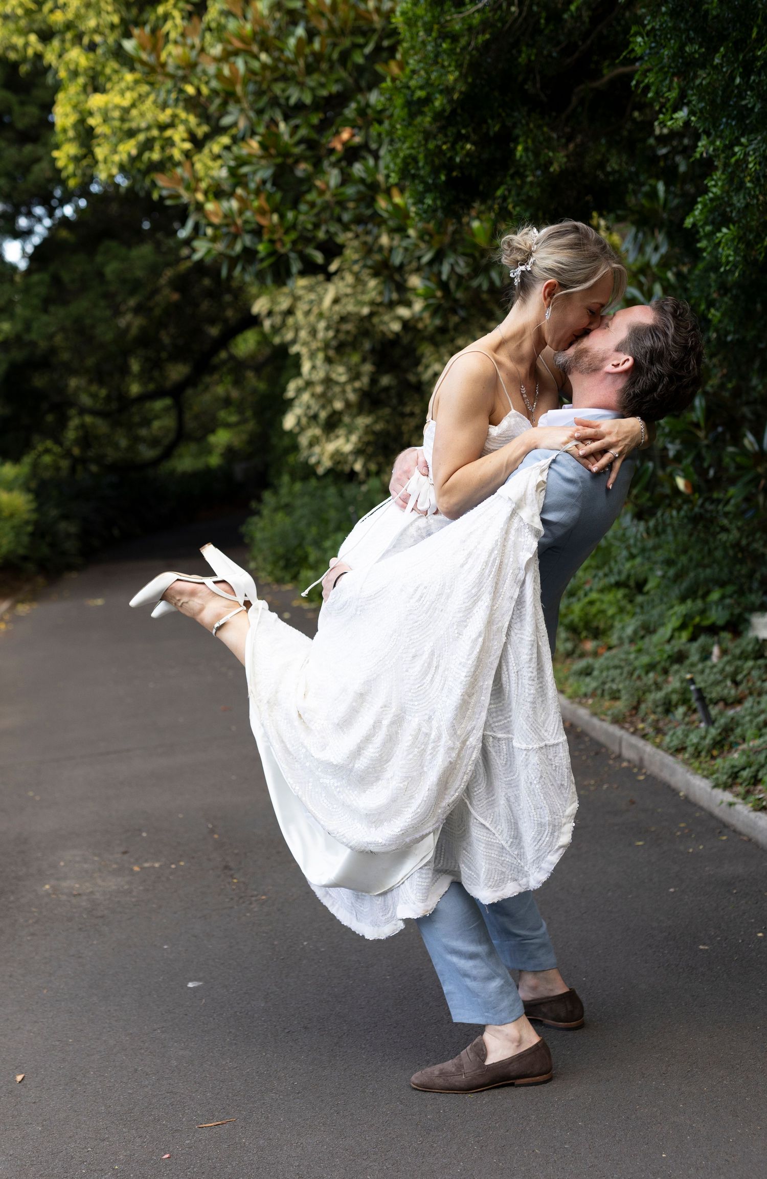 Romantic dip pose on garden path with bride in flowing white dress.