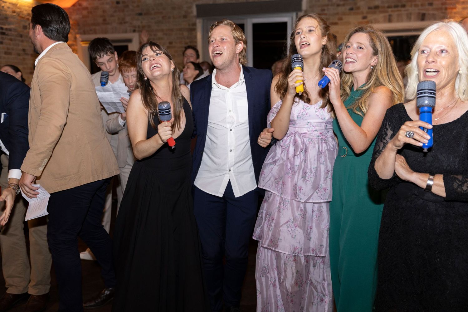 Wedding guests dancing and celebrating together at reception with brick wall backdrop.