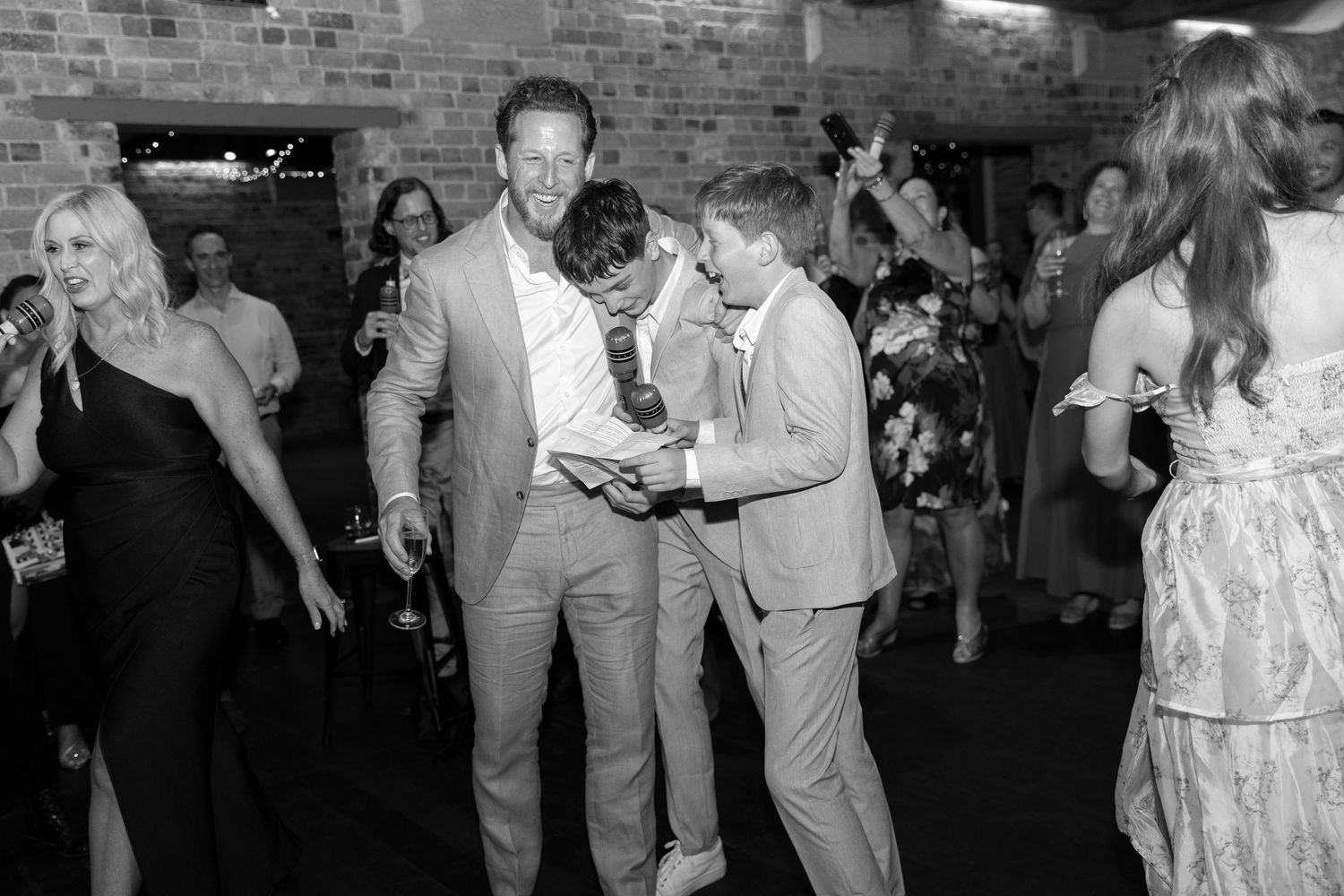 Wedding reception guests dancing and celebrating in brick-walled venue.
