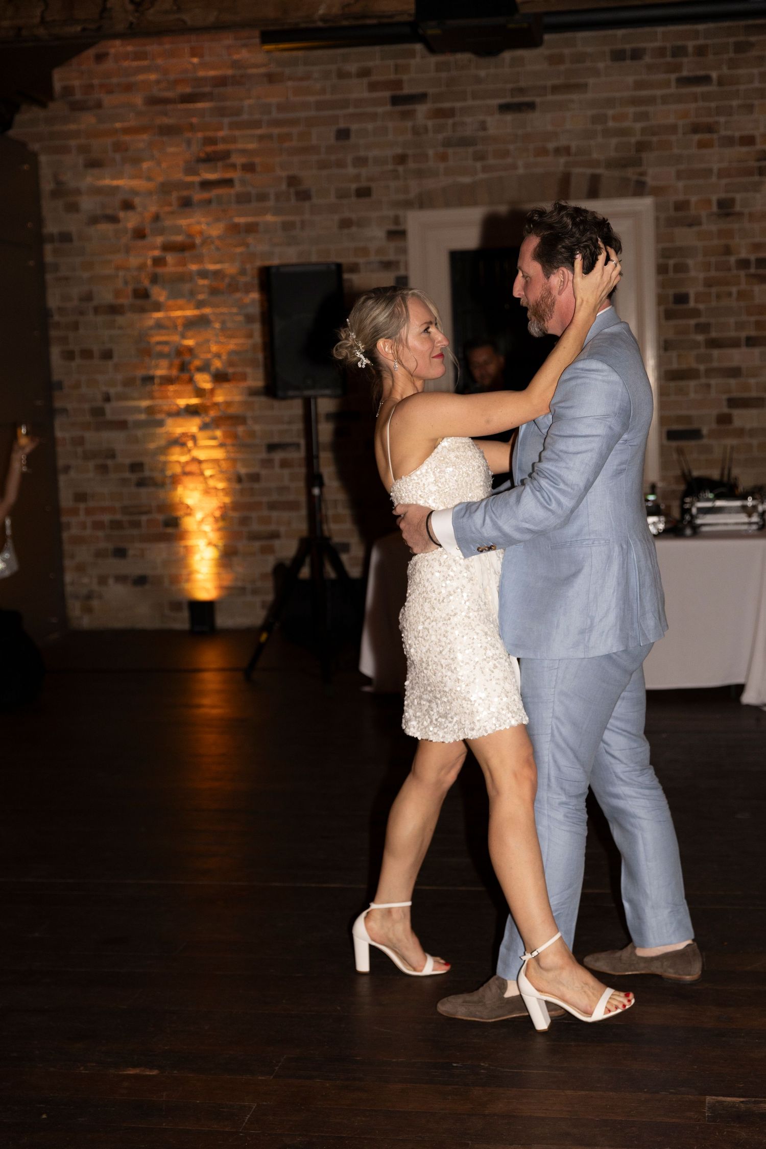 Wedding couple dancing together in venue with romantic amber lighting and exposed brick walls.