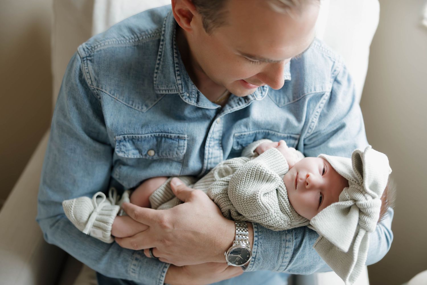 A tender moment captured between parent and newborn baby in denim jacket against soft natural lighting.
