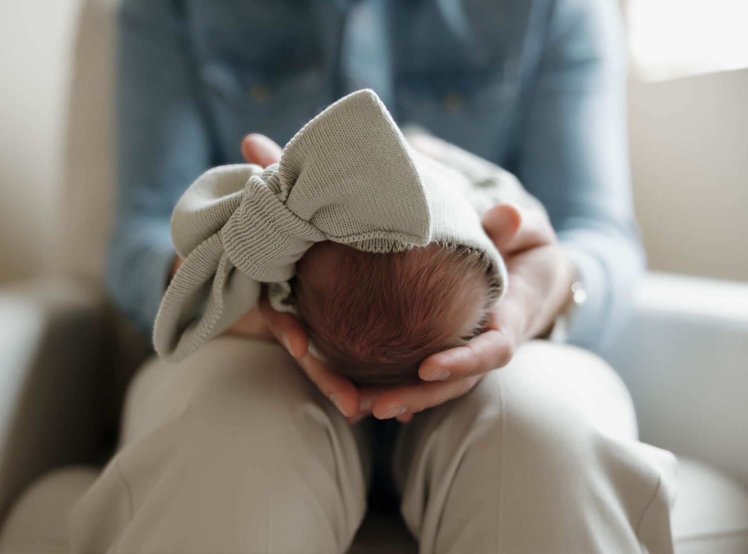 Close up view of a newborn baby's head with a bow headband being gently cradled in someone's hands.