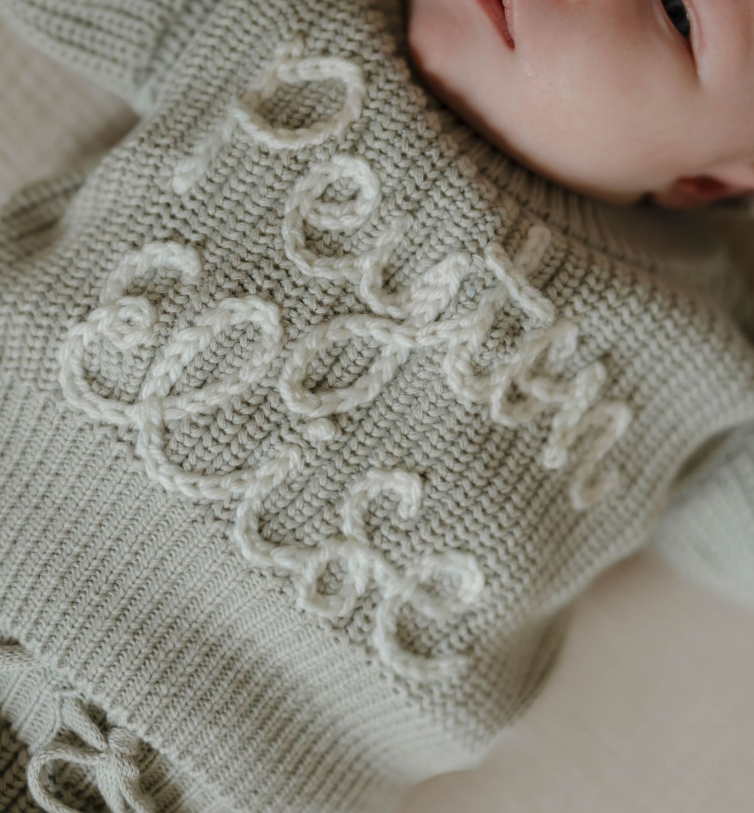 Close-up of delicate knit fabric with intricate lace pattern details in soft beige color.