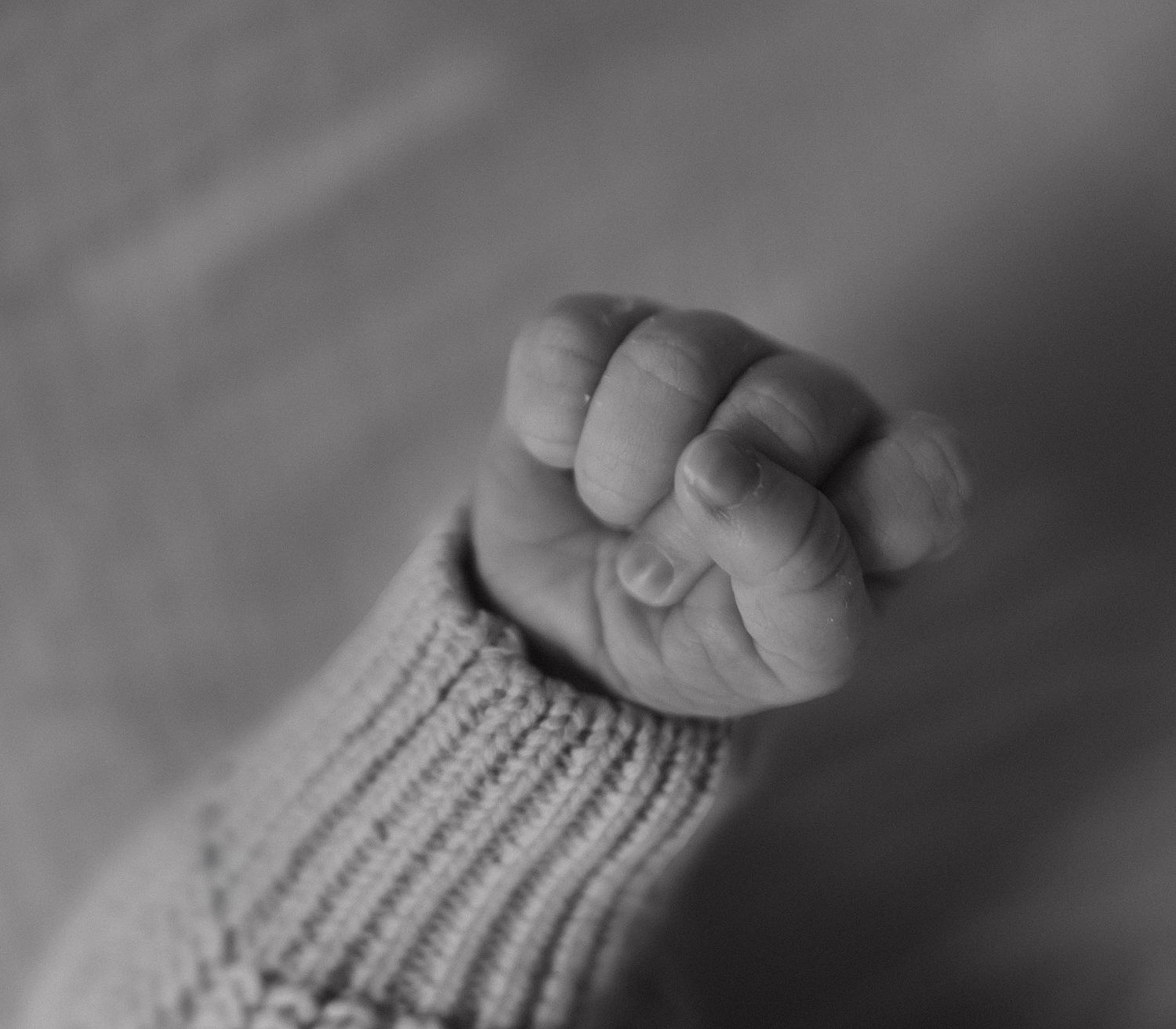 A close-up black and white photo shows a baby's tiny hand grasping an adult's finger.
