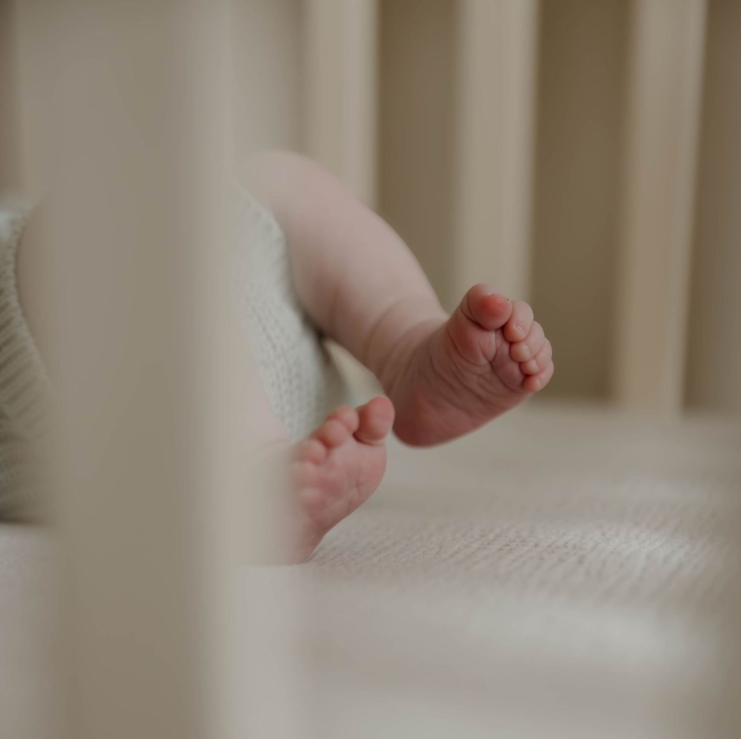 Baby's tiny feet resting on white bedding with natural window light streaming in.