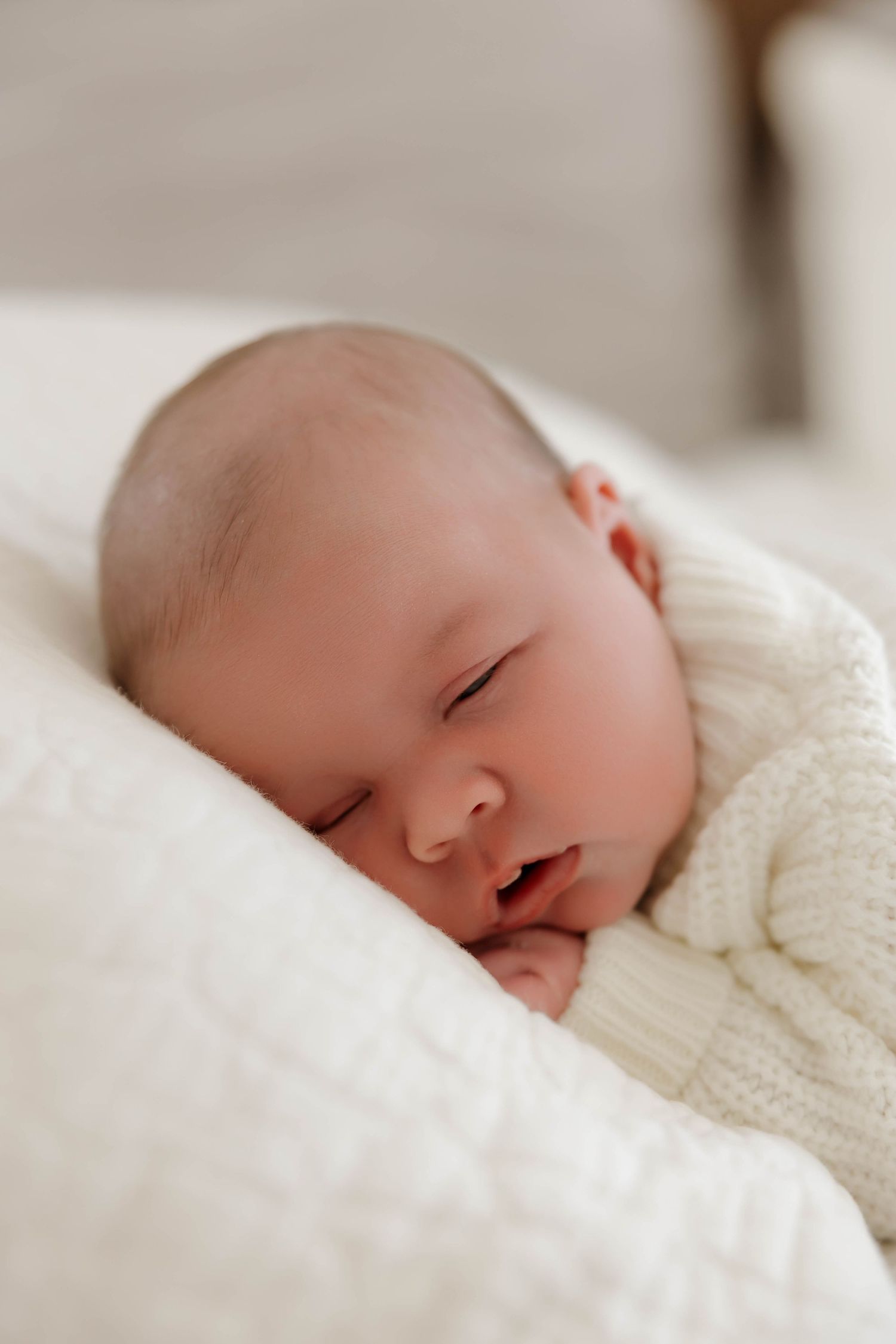 A peaceful sleeping baby wrapped in a cozy white knit blanket rests on soft bedding.