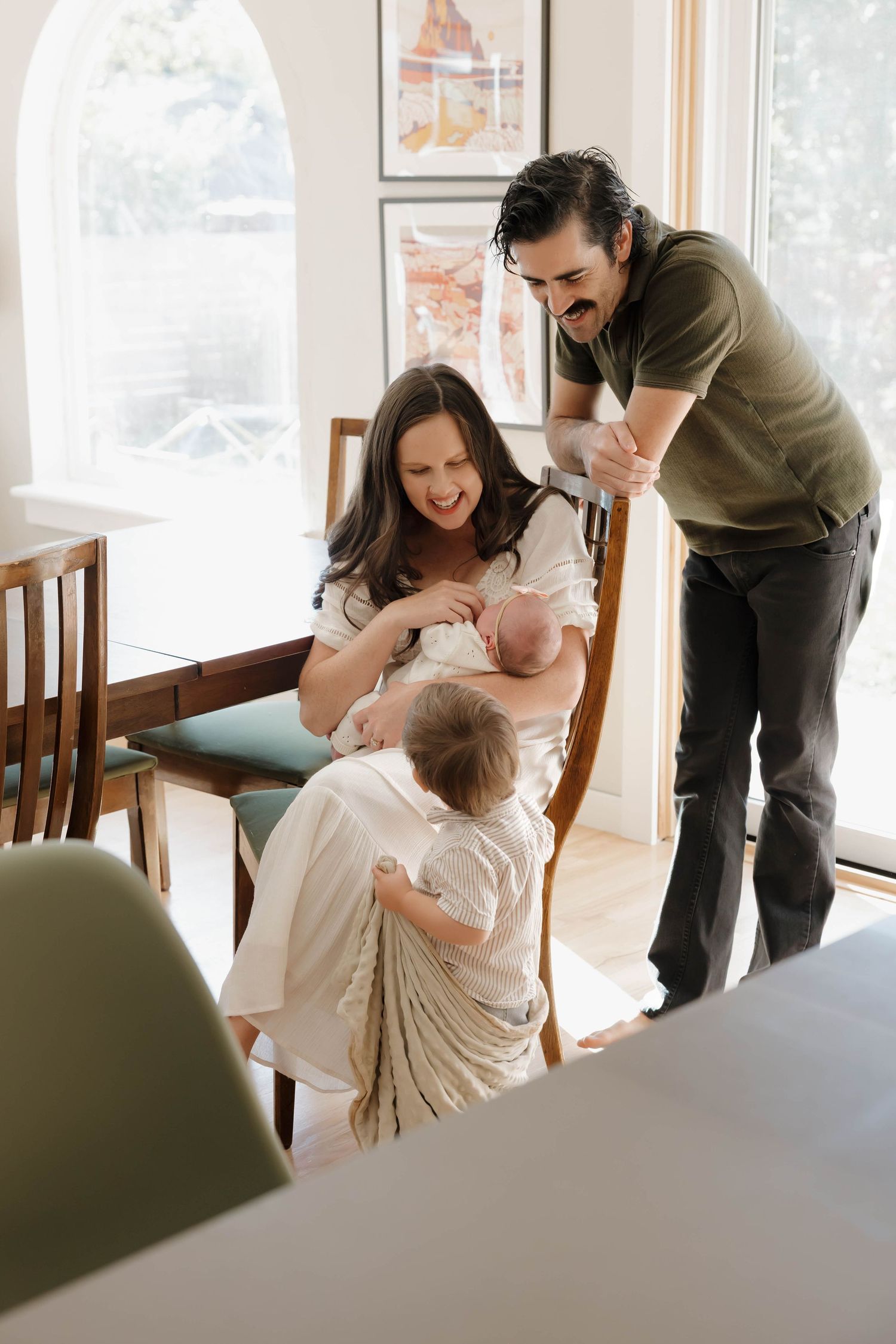 A sequence of five intimate family moments showing parents playing with their baby in a bright, sunlit dining room.